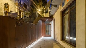 A narrow hallway with a wooden door at the end, a staircase to the left, and a building facade on the right. - Mirotza Rooms (Orio)