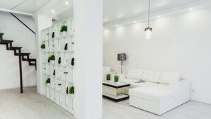 Una sala de estar moderna con un sofá blanco, una mesa de centro y una escalera con pared y estantes blancos.