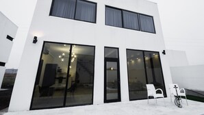 Un edificio moderno de dos pisos con grandes puertas y ventanas de vidrio, una escalera que conduce al piso superior y una bicicleta estacionada afuera.