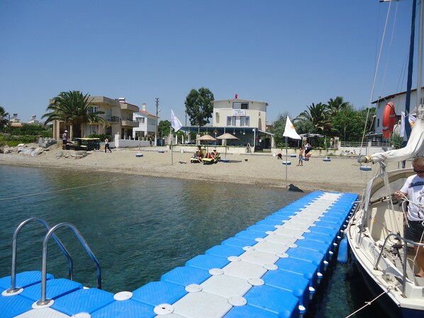 A pier with a blue and white deck, a boat docked at the end, and a beach with buildings and palm trees in the background.