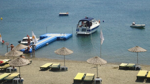 Una playa con tumbonas, sombrillas y un muelle con barcos.