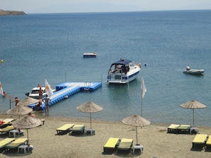 Una playa con tumbonas, sombrillas y un muelle con barcos.
