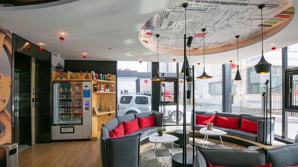 A modern interior with a curved ceiling, a seating area with red cushions, a vending machine, and a view of the street.