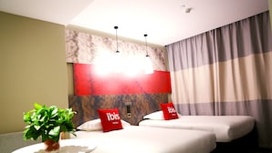 A hotel room with two beds, a small table with a plant, and a wall-mounted light fixture.