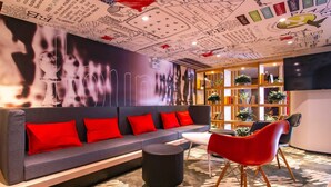 A modern lounge area with a grey sofa, red cushions, a black ottoman, and a red chair. - Ibis Wuxi Taihu Square Hotel (Wuxi)