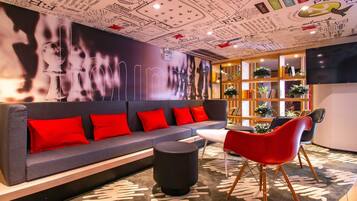 A modern lounge area with a grey sofa, red cushions, a black ottoman, and a red chair.