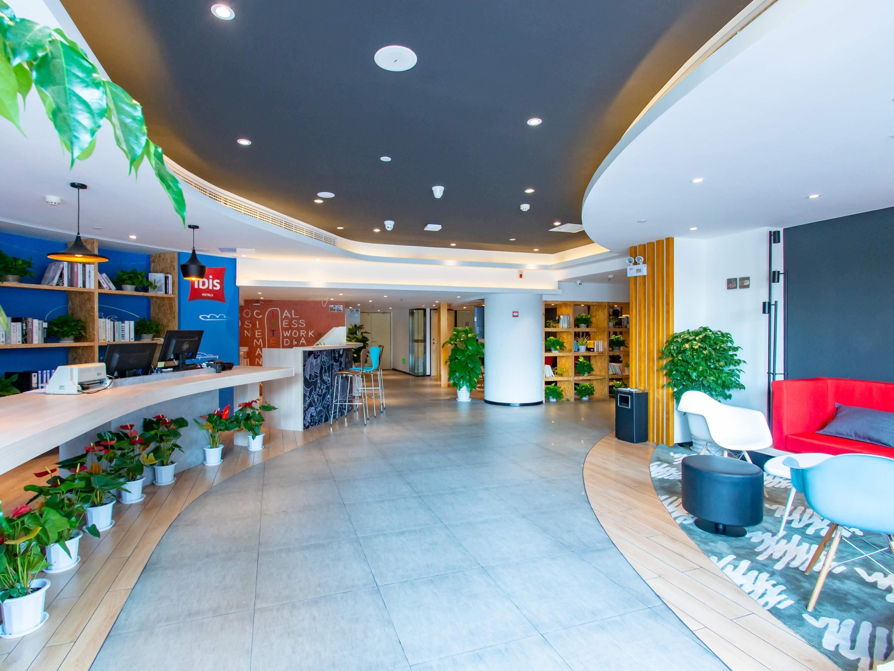 A modern hotel lobby with a reception desk, seating area, and a large bookshelf.