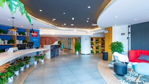 A modern hotel lobby with a reception desk, seating area, and a large bookshelf. - Ibis Wuxi Taihu Square Hotel (Wuxi)