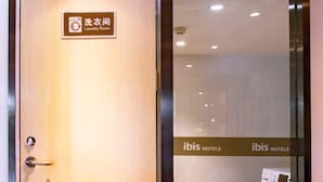 A hotel room entrance with a wooden door, a sign indicating a laundry room, and a glimpse of a washing machine inside. - Ibis Wuxi Taihu Square Hotel (Wuxi)