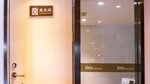 A hotel room entrance with a wooden door, a sign indicating a laundry room, and a glimpse of a washing machine inside.