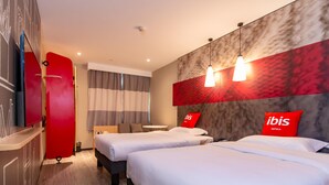 A hotel room with two beds, a TV, a desk, and a window with curtains.