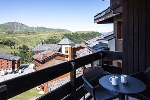 A balcony with a table and chairs, overlooking a mountainous landscape with buildings. - Terresens - Le Centaure (La Plagne-Tarentaise)