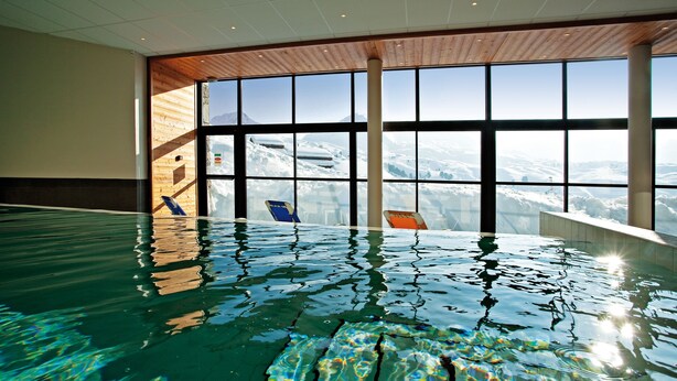 An indoor swimming pool with a view of snow-covered mountains through large windows.