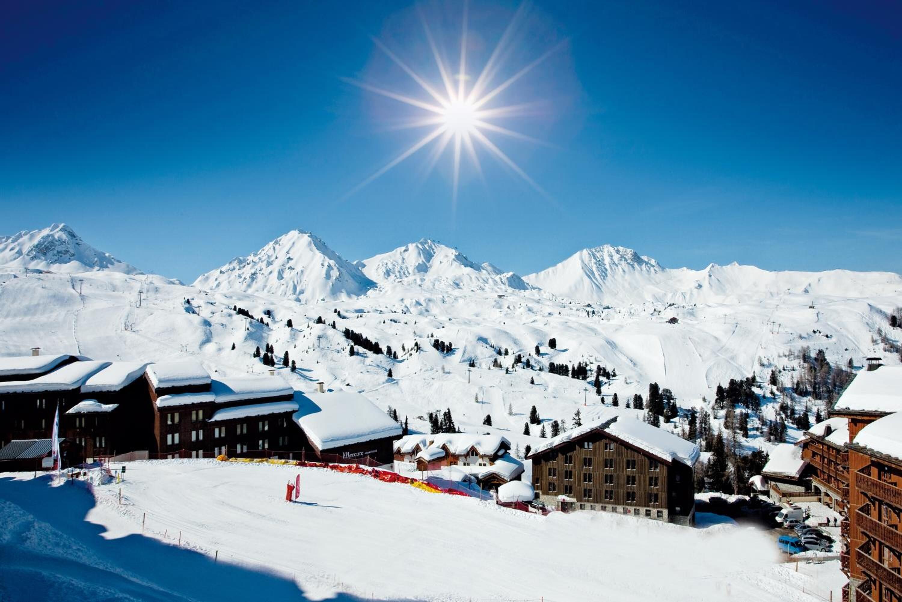 Estância de montanha coberta de neve com vários edifícios, incluindo uma hospedaria com telhado coberto de neve e um prédio maior com uma placa que diz 'Motel'.