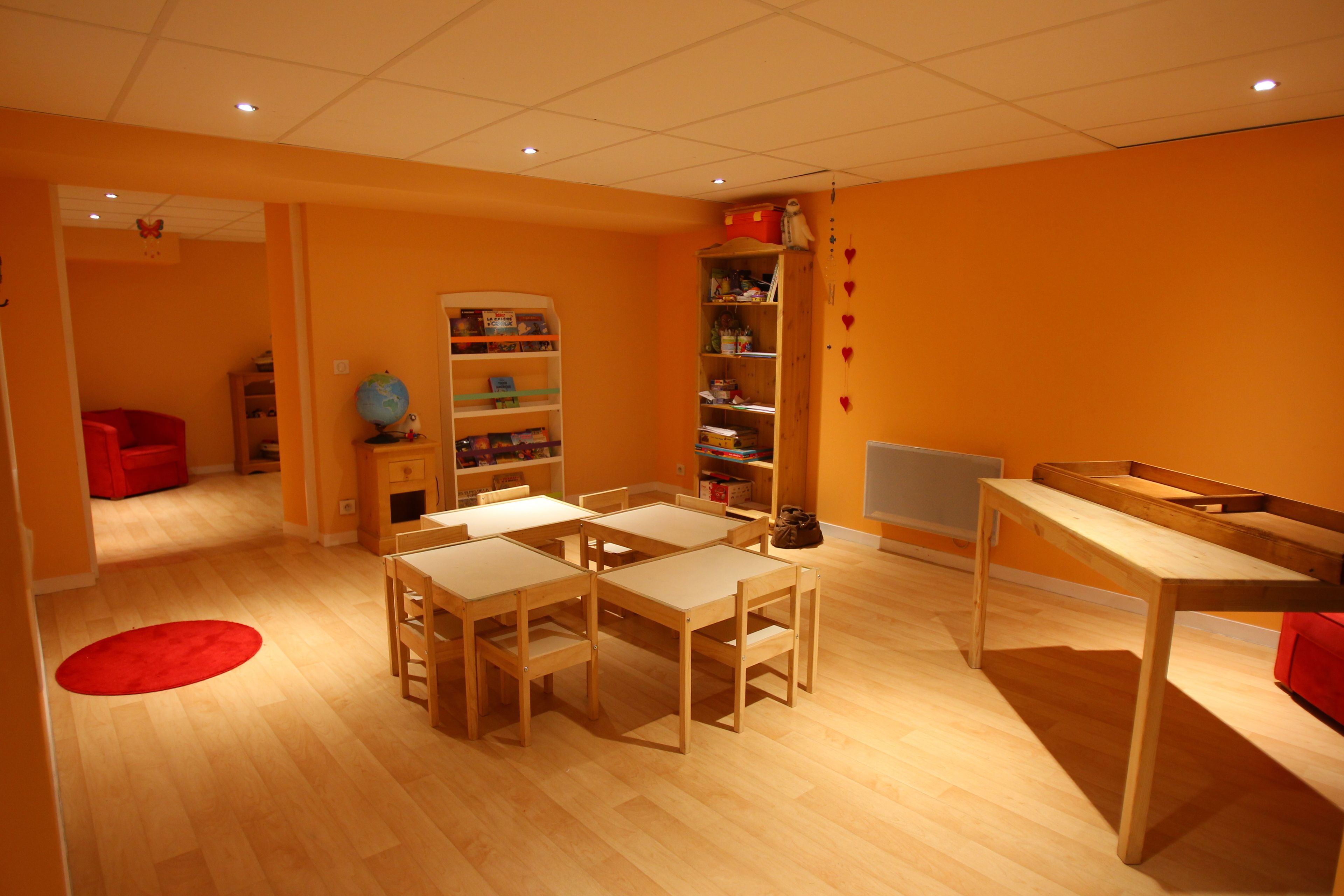 A room with a wooden floor, a red chair, a wooden table, and a bookshelf.