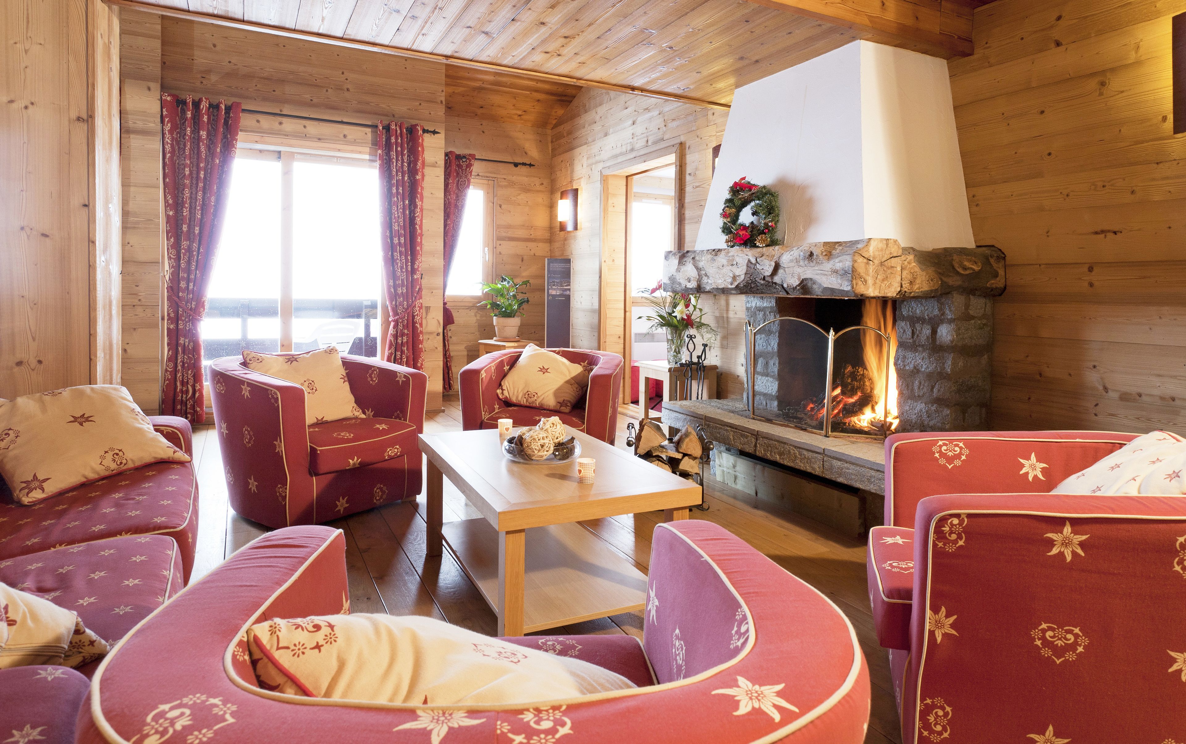 A cozy log cabin interior with wooden walls, a stone fireplace, and red upholstered furniture.