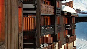 A multi-story wooden building with balconies, set against a snowy mountain backdrop.