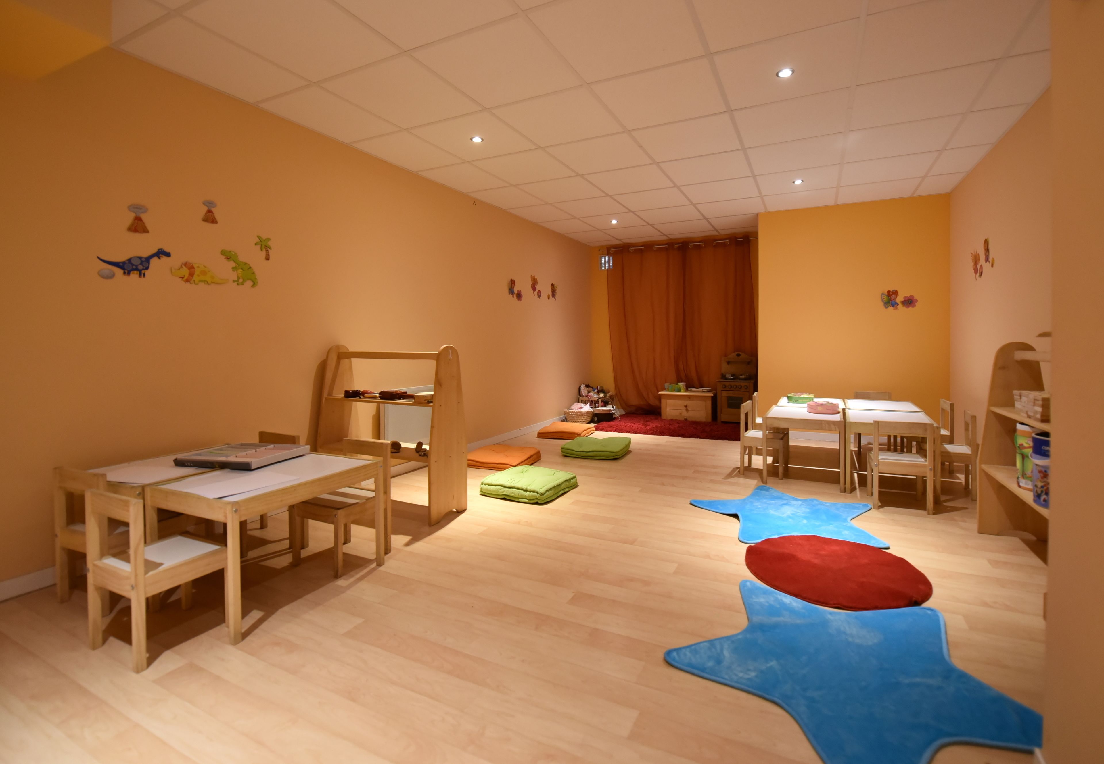 Un salón de juegos para niños con muebles de madera, piso alfombrado y decoraciones en las paredes.