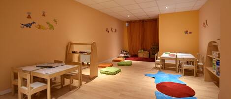 Un salón de juegos para niños con muebles de madera, piso alfombrado y decoraciones en las paredes.