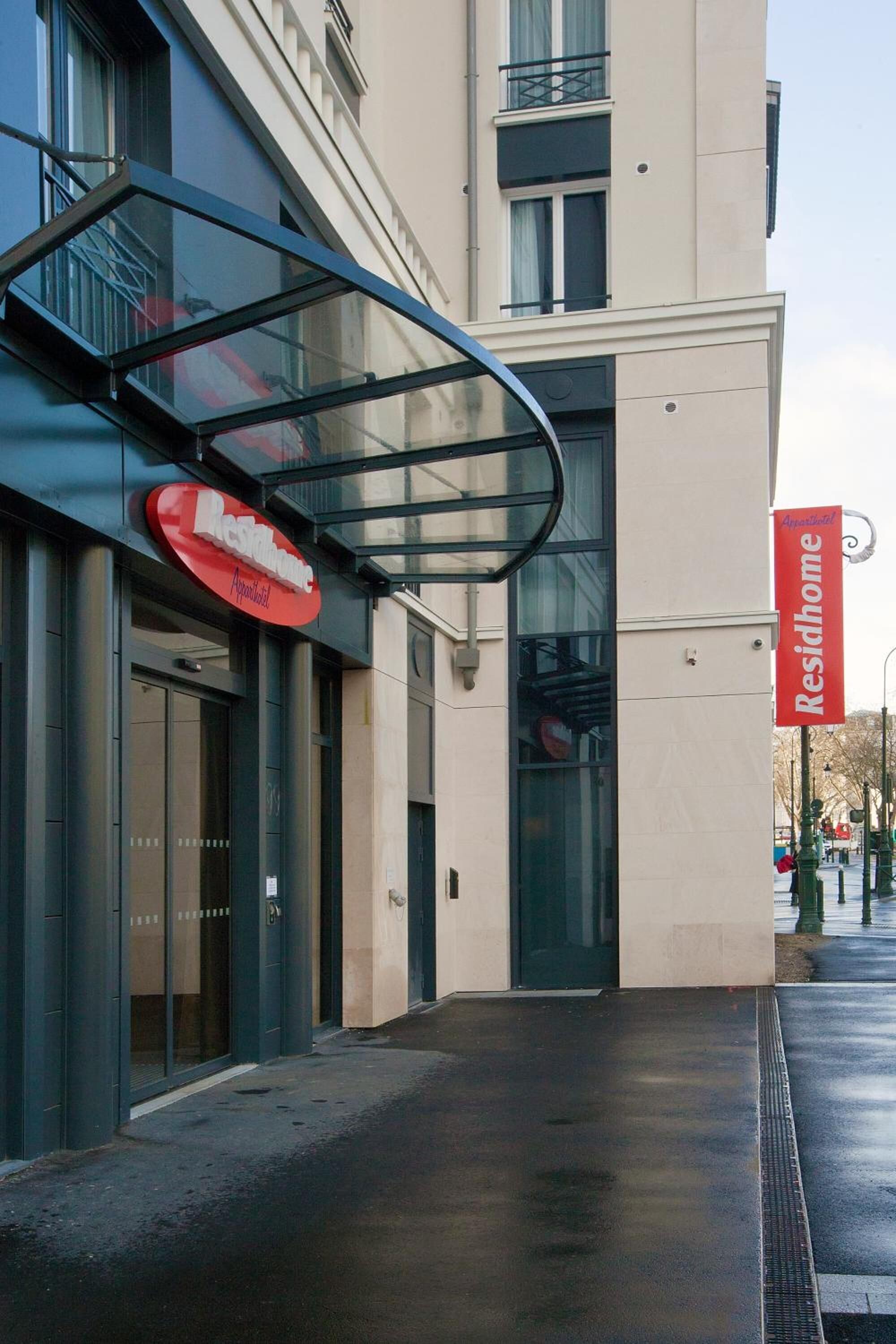A building with a glass entrance canopy and a red sign indicating a restaurant.