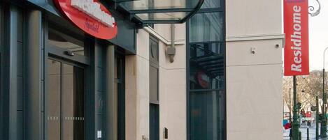 A building with a glass entrance canopy and a red sign indicating a restaurant.