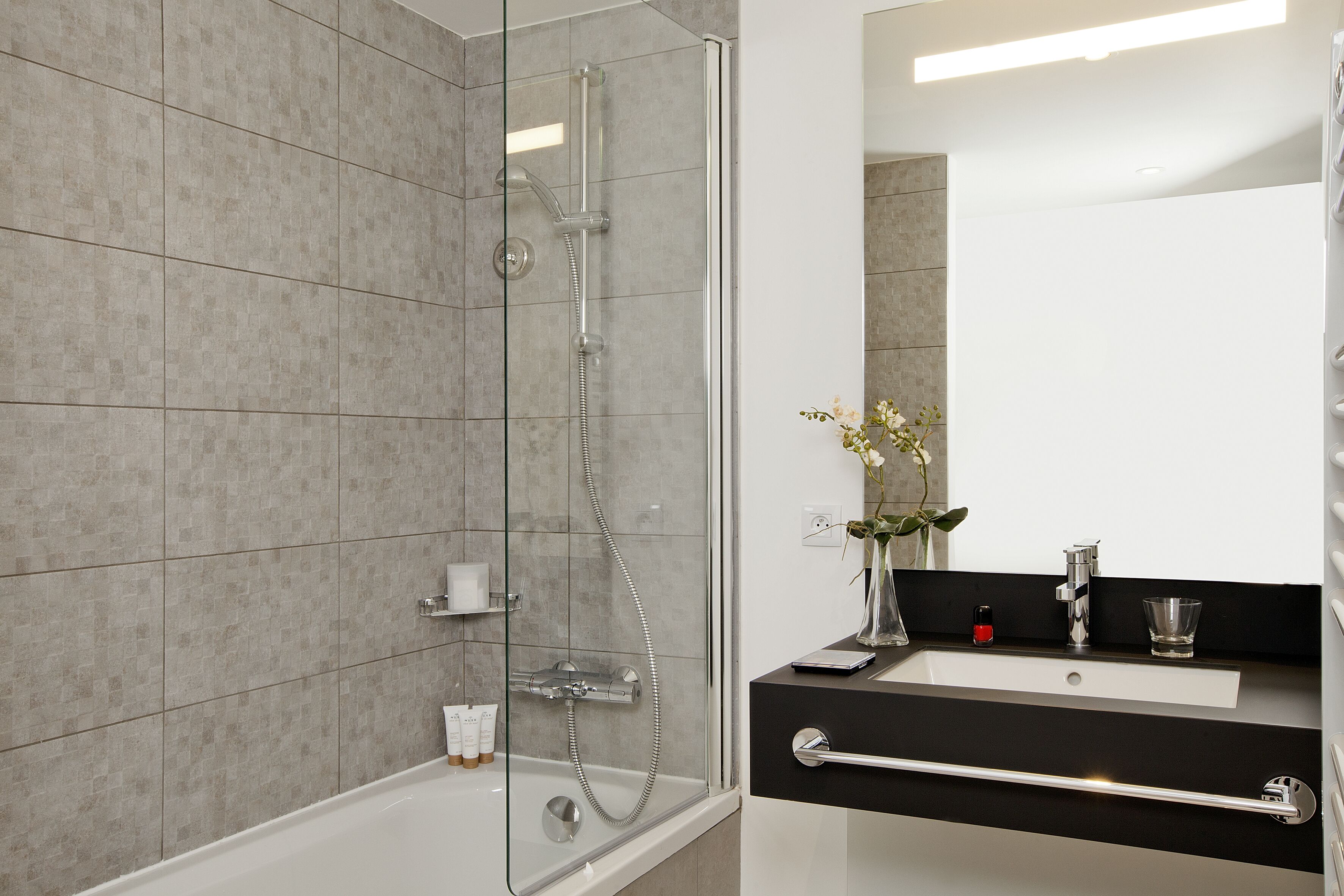 Une salle de bain moderne avec une douche à parois de verre, un lavabo blanc et un miroir au-dessus.