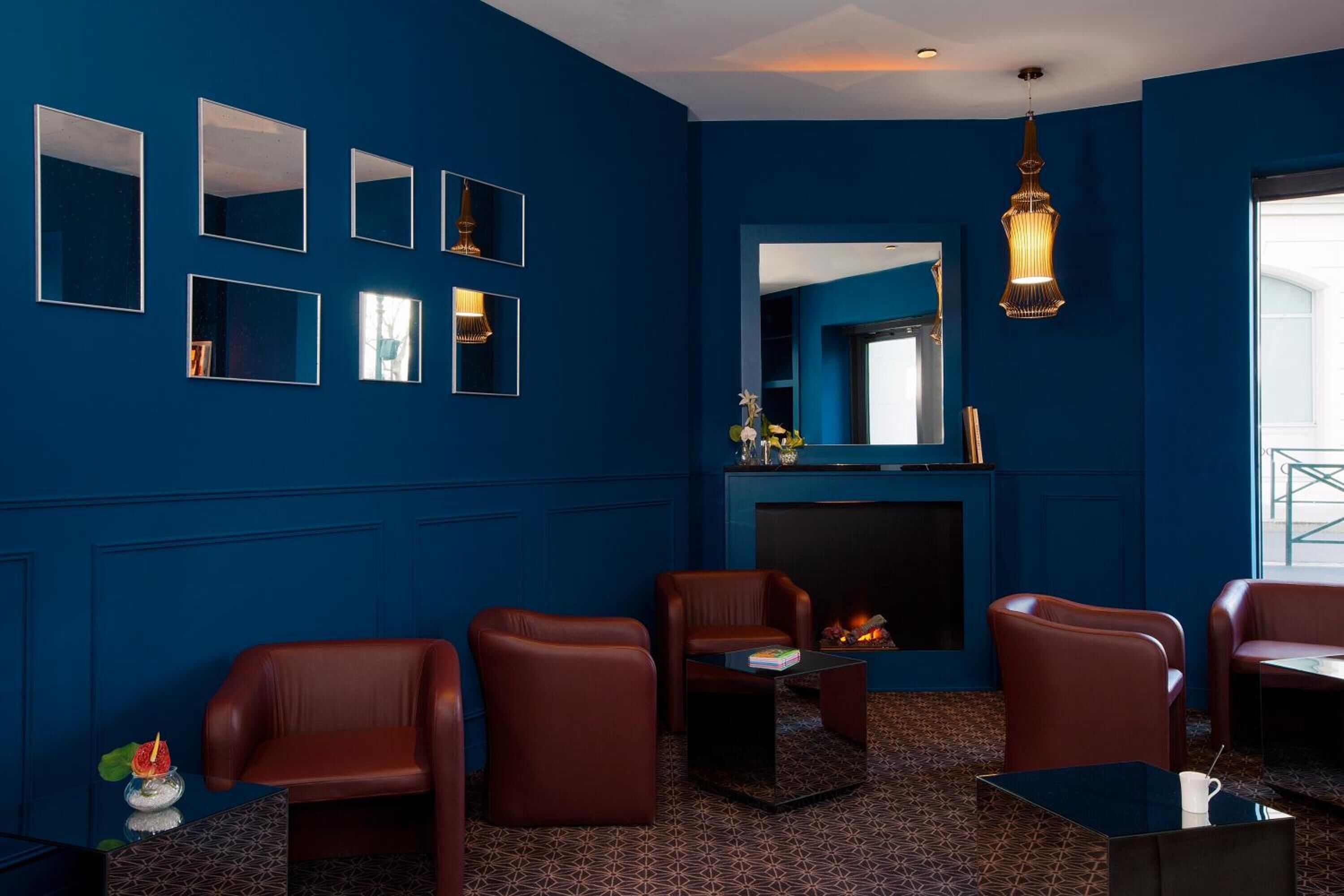 A room with blue walls, multiple mirrors, leather chairs, a fireplace, and a hanging light fixture.