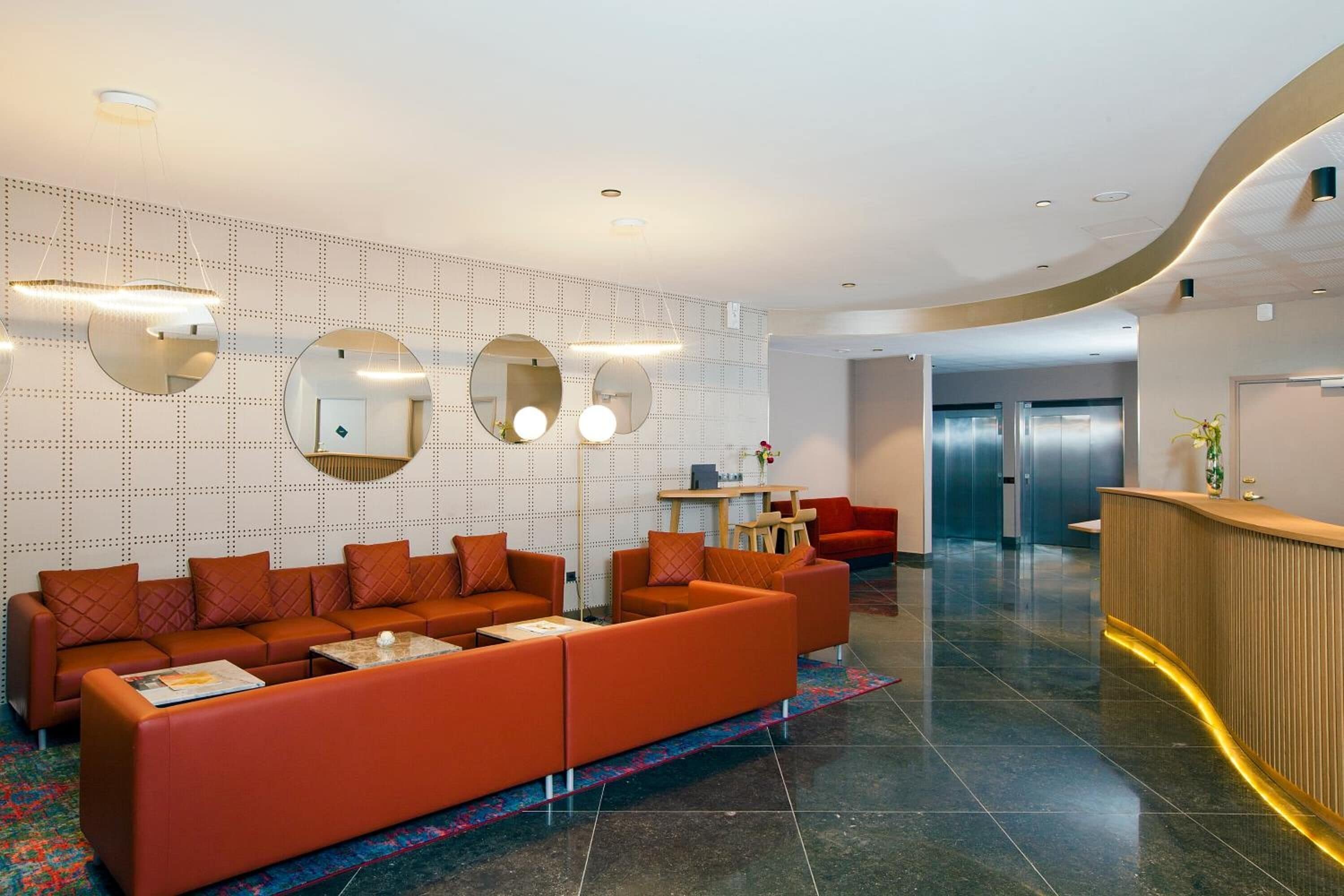 A modern lobby with a sectional sofa, a reception desk, and a patterned wall.