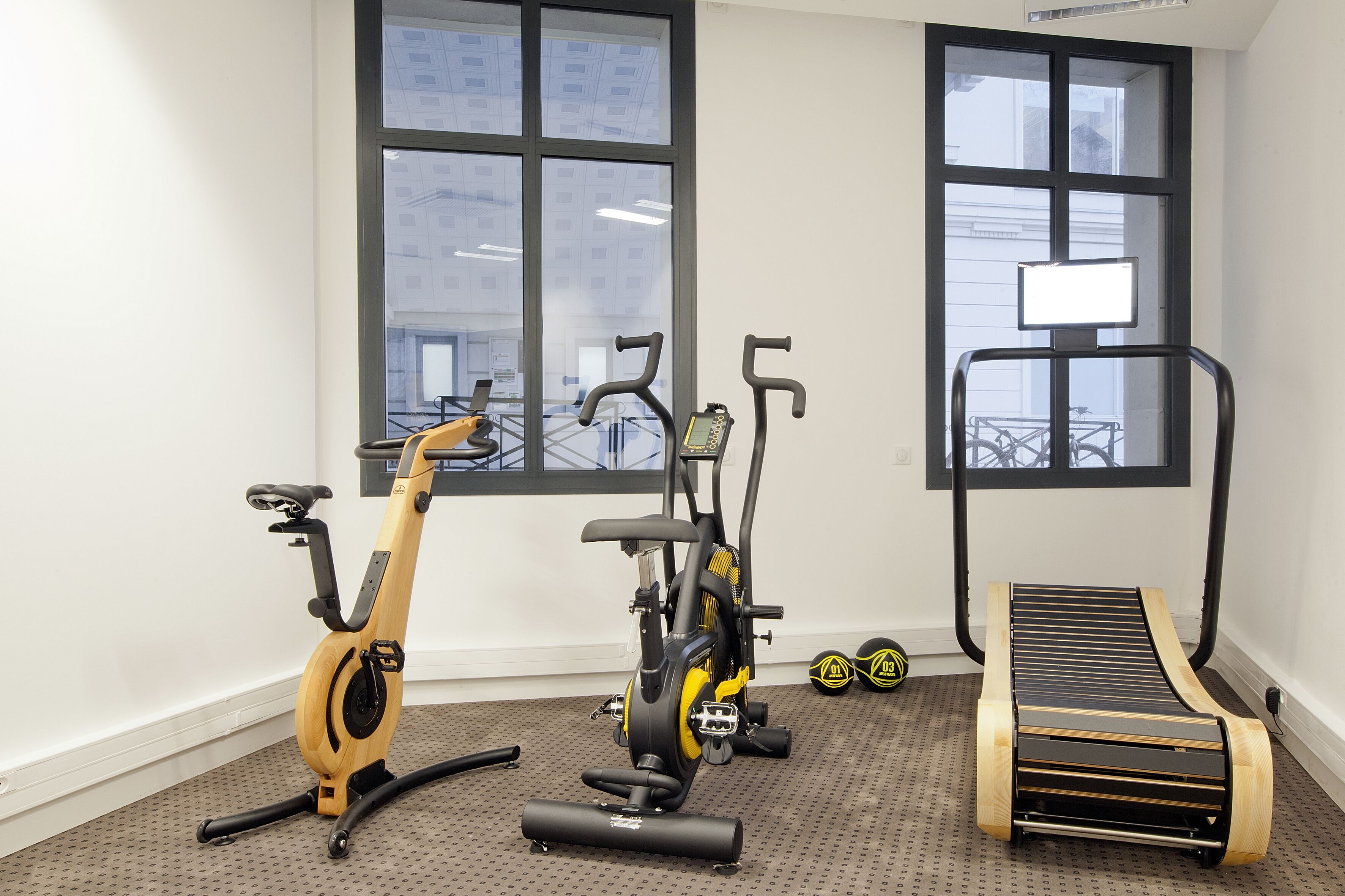 Une salle de sport équipée d’un vélo d’exercice, d’un appareil elliptique, d’un tapis de course et de poids.