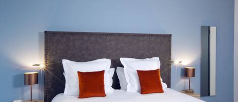 A neatly made bed with white and brown pillows, two bedside lamps, and a nightstand with a book.