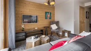 Un salon moderne avec un mur en bois, un canapé gris, un téléviseur et une petite table en bois sur laquelle se trouvent un bol et une tasse.