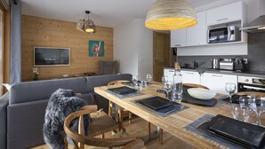 Une cuisine moderne avec des meubles blancs, un four à micro-ondes et une bouilloire. On y trouve une table à manger mise avec des assiettes, des verres et des couverts.
