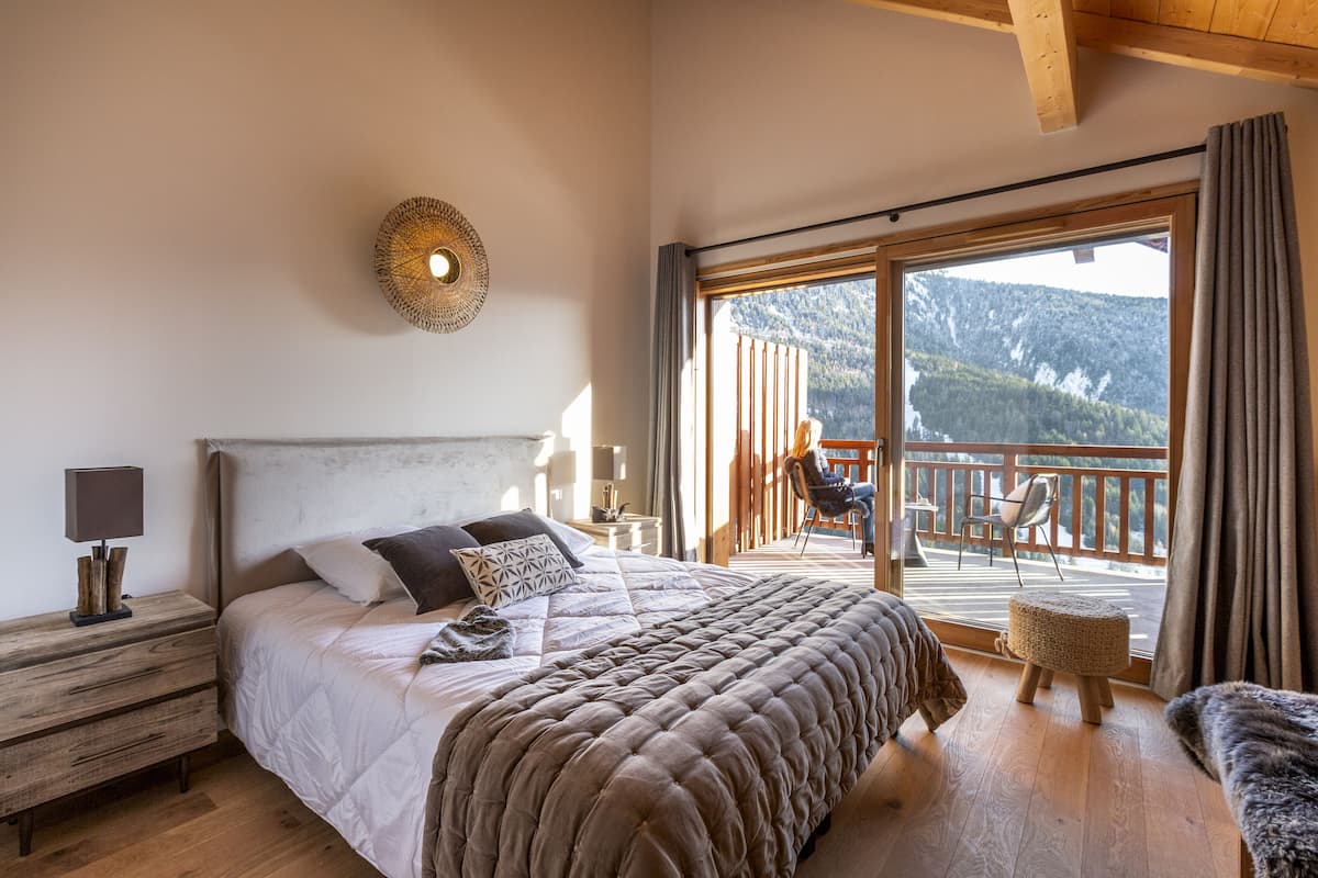 Une chambre dotée d’un grand lit, d’une table de chevet, d’une lampe et donnant sur un balcon aménagé avec du mobilier d’extérieur.