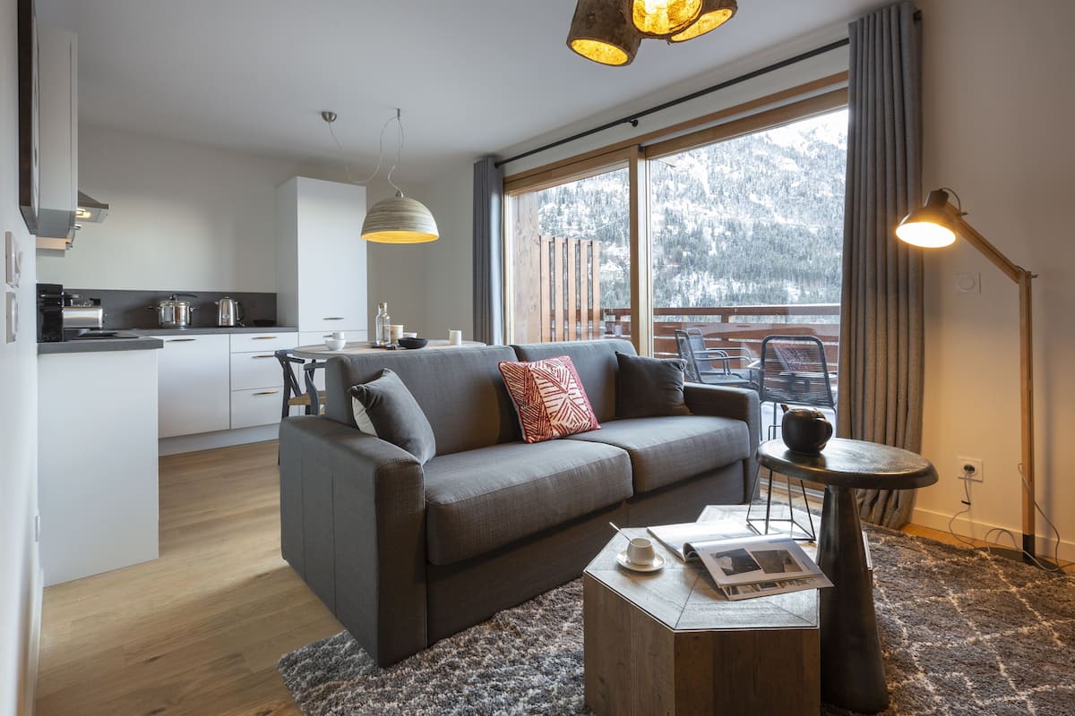 Un salon moderne avec un canapé gris, une table basse et une vue sur un paysage enneigé par de grandes fenêtres.