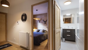 Une chambre à coucher comprenant un lit, un radiateur et une porte donnant sur une salle de bain équipée d’un miroir et d’un lavabo.