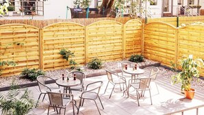 Un espace extérieur aménagé en terrasse, avec des tables et des chaises rondes, entouré d’une clôture en bois et agrémenté de plantes en pot.