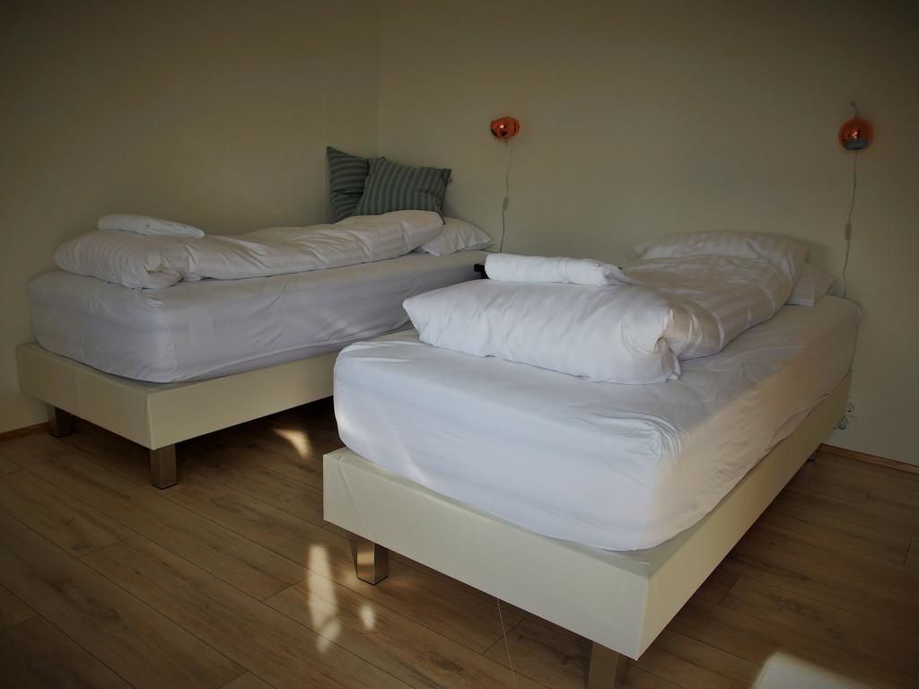 Twee enkele bedden met witte beddengoed in een kamer met houten vloer.
