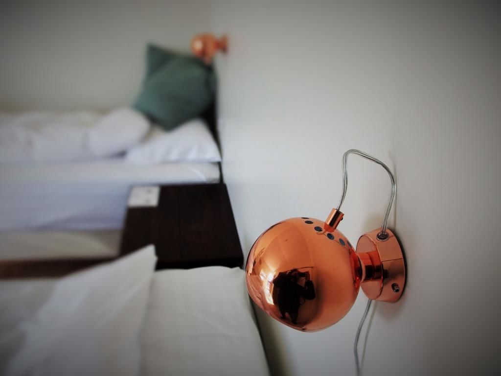 Una habitación con una cama, una mesita de noche y una lámpara de pared.