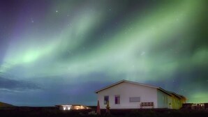 Una casa con facciata bianca e un piccolo portico, sotto un cielo notturno con stelle visibili e aurora boreale.
