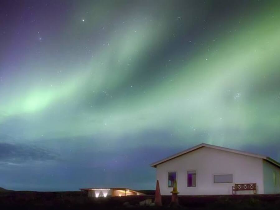 A house with a white exterior and a small porch, under a night sky with visible stars and aurora borealis.