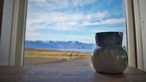 Un vaso di metallo su un davanzale con vista su un paesaggio che include montagne e un lago.