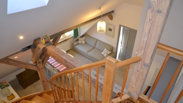 A wooden staircase leading to a loft bedroom with a sloped ceiling, a sofa with 'LOVE' pillows, and a hanging light fixture. - Grand Apartments - Loft (Sopot)