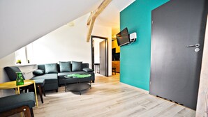 A modern living room with a sofa, coffee table, and chairs. There is a television mounted on the wall and a door leading to another room. - Grand Apartments - Loft (Sopot)