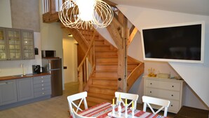 A modern kitchen with wooden staircase, white dining table, and a flat-screen TV. - Grand Apartments - Loft (Sopot)