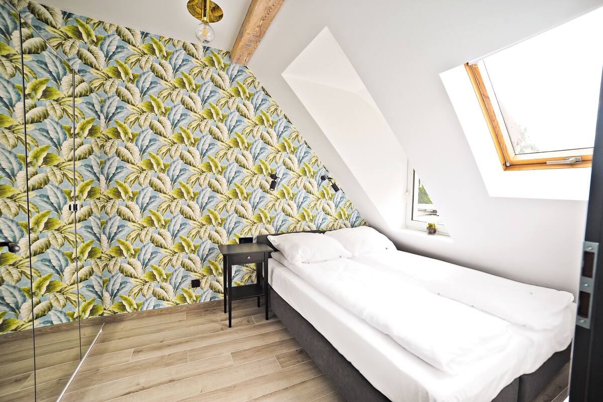 A bedroom with a bed, a small table, a wall with a leaf pattern, and a skylight.