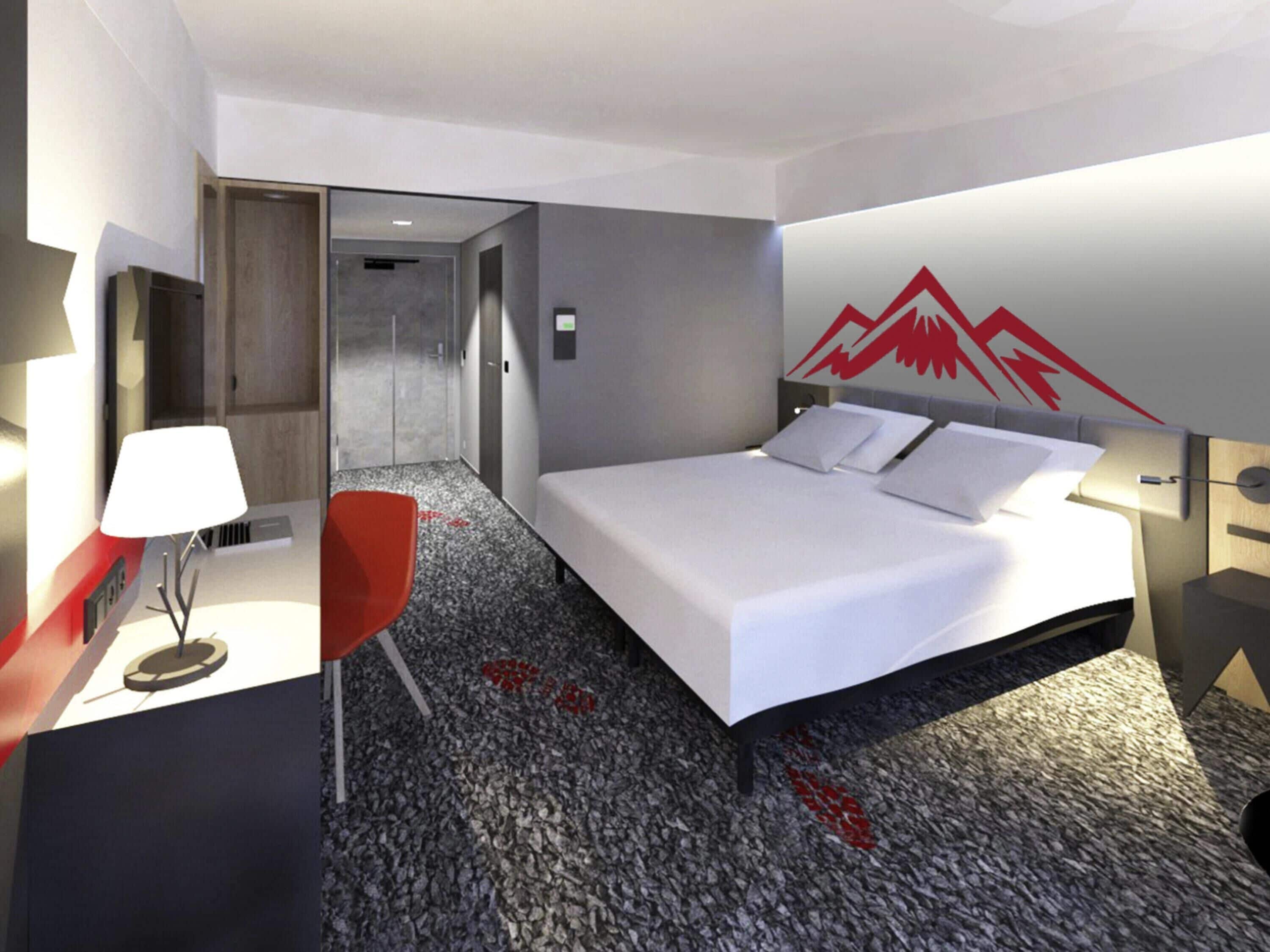 A hotel room with a bed, a desk, a chair, and a red wall decoration.
