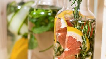 A close-up of a glass bottle with a cork stopper, containing a liquid, slices of lemon, rosemary, and a piece of meat, likely prosciutto.