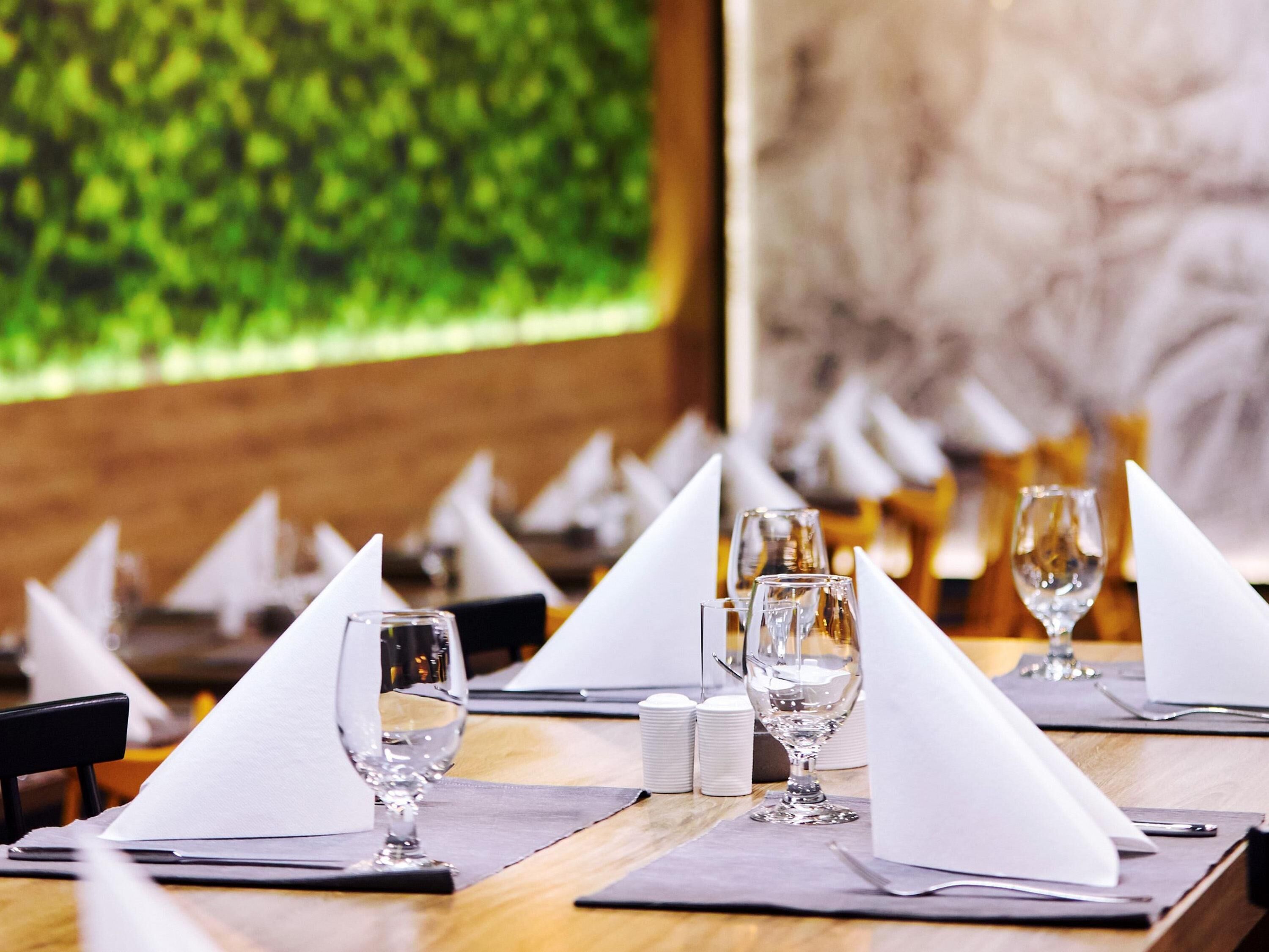Un ambiente de restaurante con mesas dispuestas para comer, destacando cristalería transparente y servilletas dobladas.