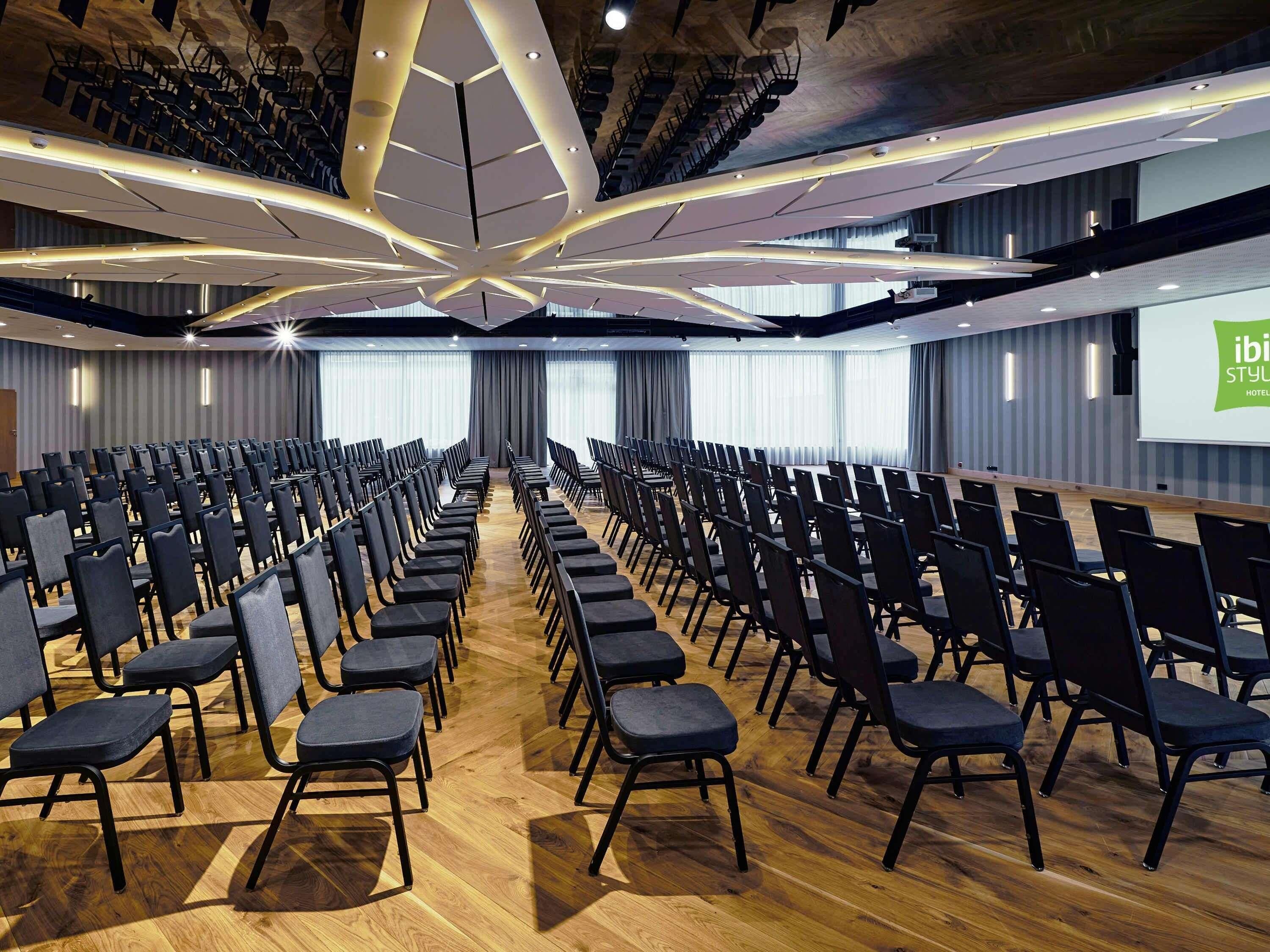A conference room with rows of chairs, a stage, and a projection screen.