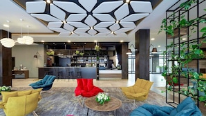 A modern lobby with a bar area, seating with colorful chairs, and a ceiling with geometric light fixtures. - ibis Styles Nowy Targ (Nowy Targ)